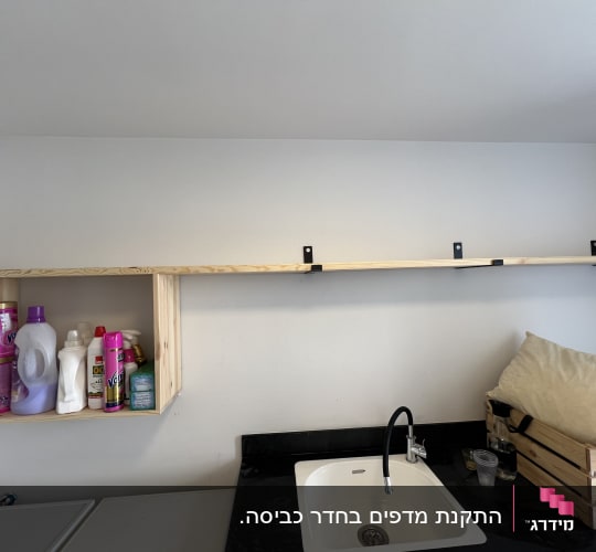 מדף עץ עם תומכים שחורים על קיר לבן